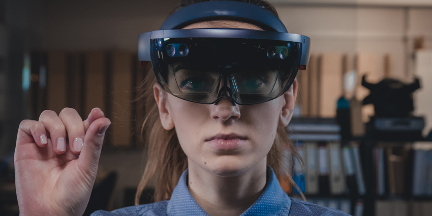 امرأة ترتدي نظارات Microsoft HoloLens وتتفاعل مع محيطها باستخدام تقنية الواقع المختلط – مثال على دمج العناصر الرقمية مع البيئة الواقعية.